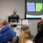 Ecology CEO Gareth Griffiths speaking at a podium in a room filled with people at the 2024 annual general meeting.