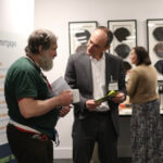 Two men talking at the Ecology annual general meeting and looking at a document which one of the men is holding.