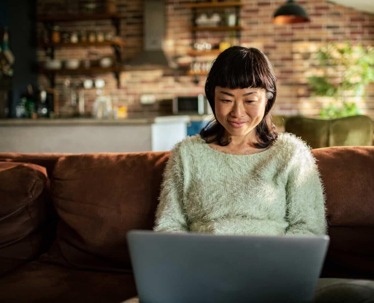 Asian woman sat in living room in front of laptop applying for an Ecology Cash ISA